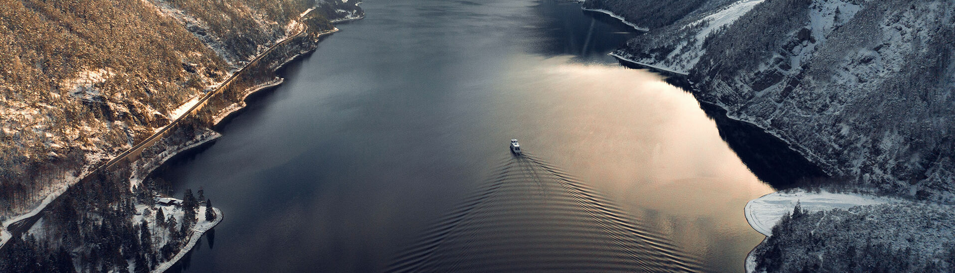 Blick auf den winterlichen Achensee, das Dorf Pertisau und das verschneite Karwendelgebirge. Auf dem Achensee fährt ein Schiff der Achenseeschifffahrt.