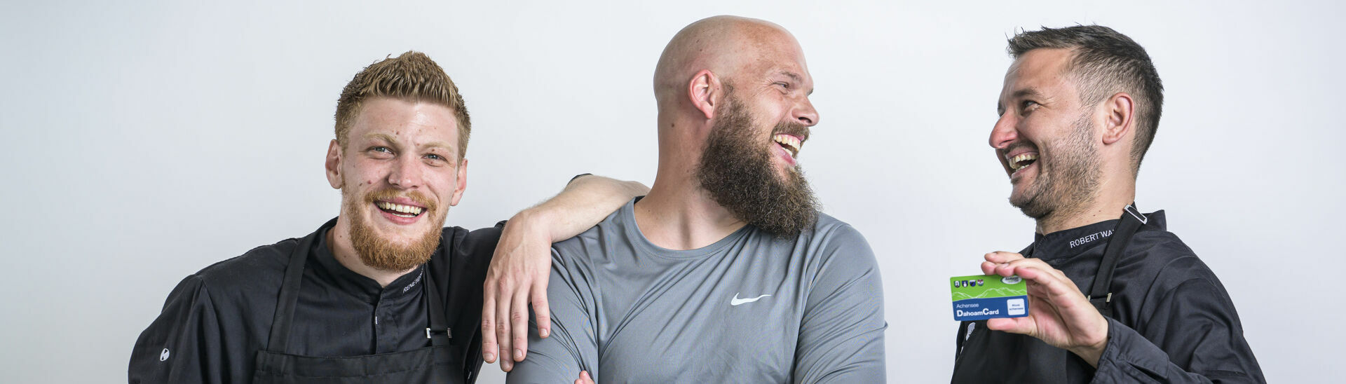 Zwei Köche und ein Fitnesstrainer posieren mit der Achensee DahoamCard vor einer weißen Wand.