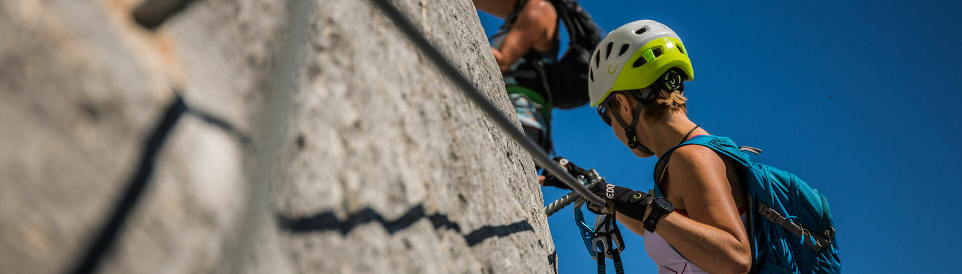 Zwei Frauen klettern an einem im Rofangebirge liegenden Klettersteig bei tollem Wetter und atemberaubendem Ausblick.
