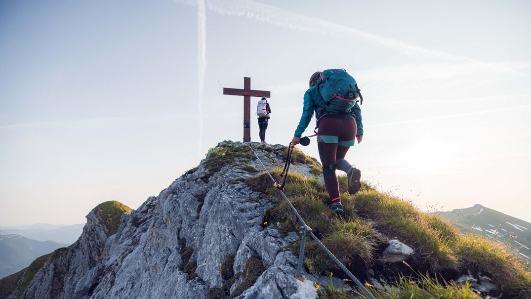 Zwei Frauen kommen gerade am Gipfelkreuz vom Rosskopf an bei schönem Wetter.