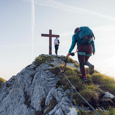 Zwei Frauen kommen gerade am Gipfelkreuz vom Rosskopf an bei schönem Wetter.