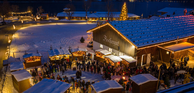Der Weihnachtsmarkt beim Fischergut erstrahlt im Lichterglanz und ist von Schnee umgeben. Zahlreiche Besucher genießen dort die Vorweihnachtszeit.