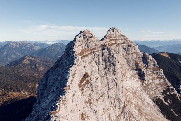 Der Guffert in Steinberg am Rofan mit einer markanten, doppelt spitzen Form, umgeben von abwechslungsreicher, bewaldeter Berglandschaft. Die Szenerie zeigt eine klare, blaue Himmel.