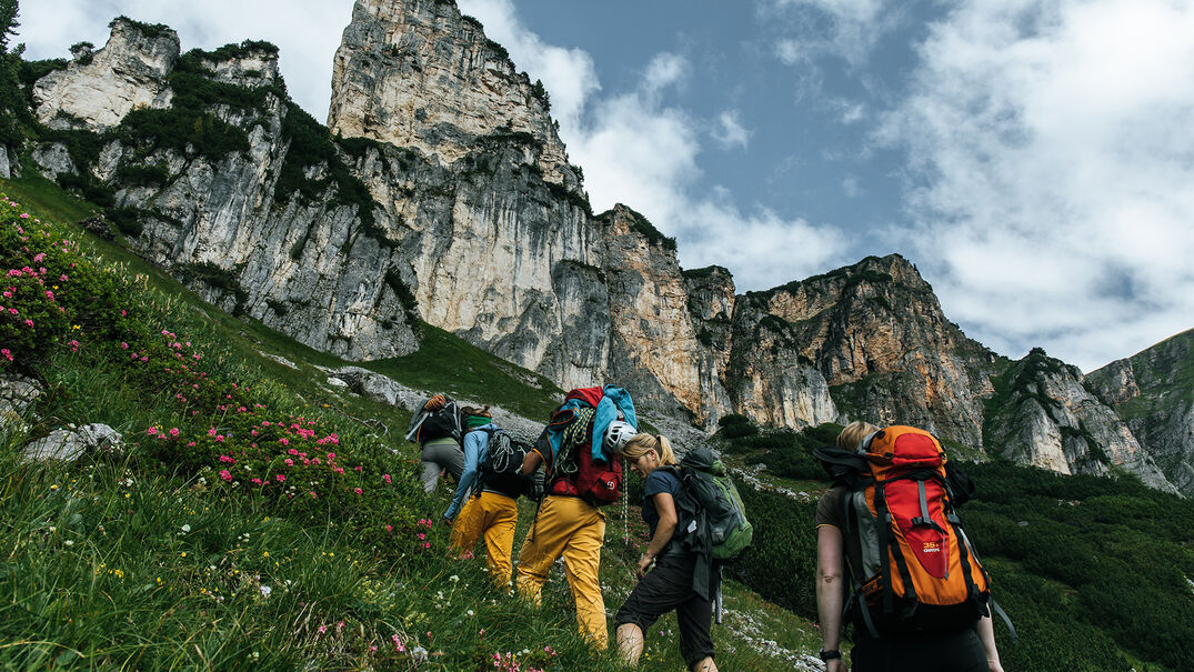 Eine kleine Gruppe aus Kletterern die mit ihrer Ausrüstung auf einen Berg im Rofangebirge wandert bei leicht bewölktem Wetter.