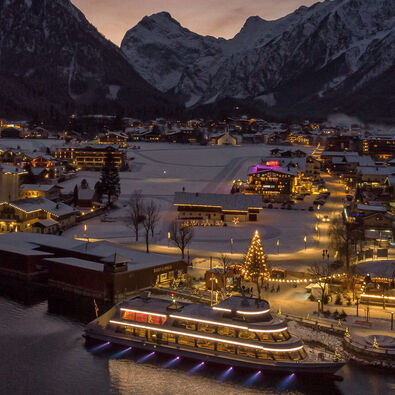 Night shot of the snow-covered village of Pertisau am Achensee in the Advent season, festooned with decorations and sparkling lights.