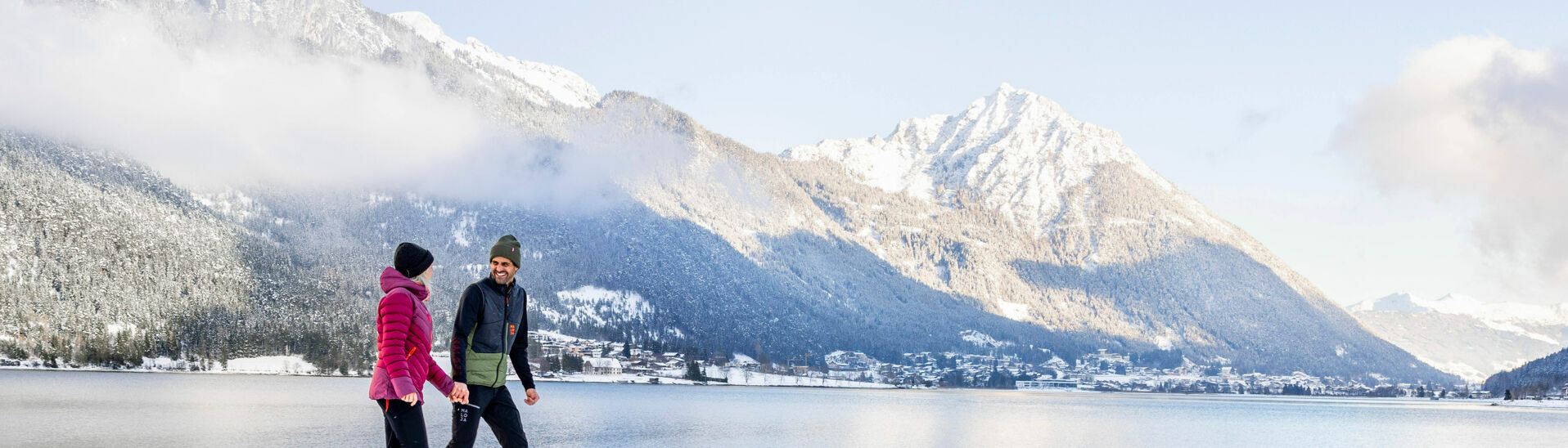 Ein Paar genießt bei einem Spaziergang die Winterlandschaft am Achensee. Im Hintergrund Maurach und das Ebner Joch.