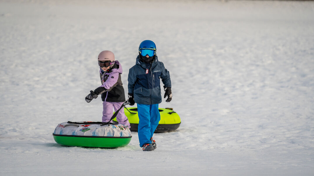 Zwei Kinder ziehen ihre Snowtubes hinter sich, nachdem sie die eigens dafür ausgewiesene Piste der Planberg- und Wiesenlifte in Pertisau hinuntergerutscht sind.