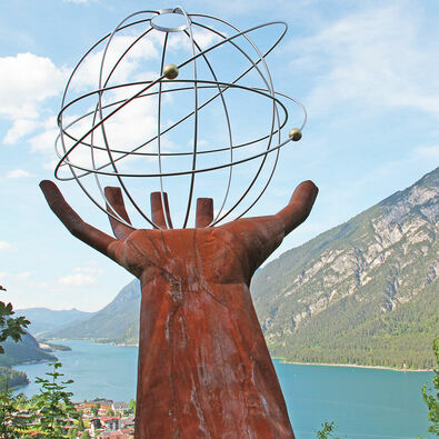 Eine Skulptur einer Hand die einen eisernen durchsichtigen Planeten auf dem Besinnungsweg am in Pertisau hält.