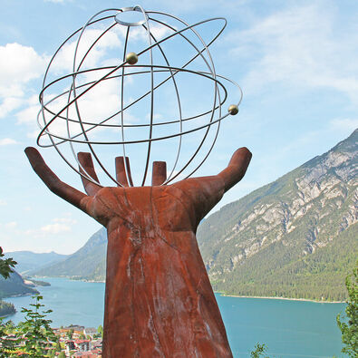 Eine Skulptur einer Hand die einen eisernen durchsichtigen Planeten auf dem Besinnungsweg am in Pertisau hält.