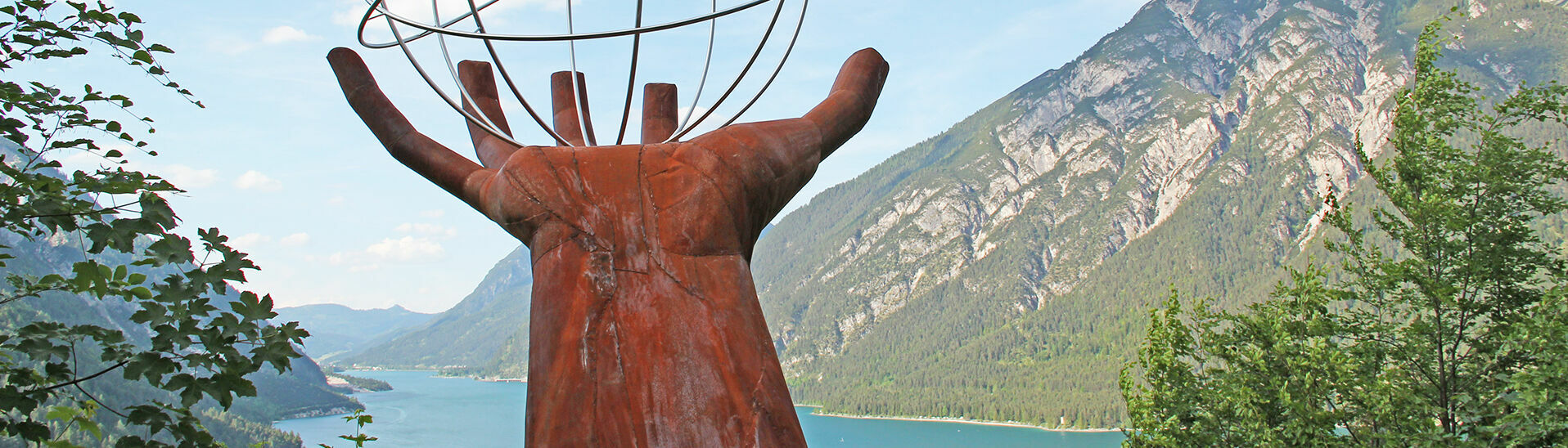 Der Besinnungsweg in Pertisau am Achensee Eine Skulptur einer Hand die einen eisernen durchsichtigen Planeten auf dem Besinnungsweg am in Pertisau hält.