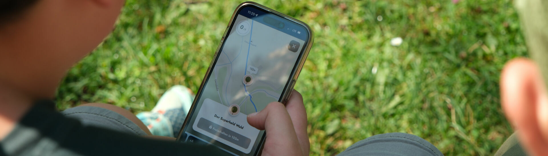 Eine Familie erkundet spielerisch mit dem Handy die wundersame Welt der Fauna und Flora des Naturparks Karwendel auf dem „Achensee Natur Erlebnispfad“.