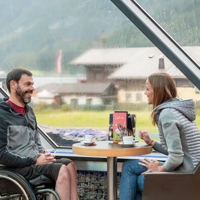 Two friends chat over a hot drink at Café Vitalberg. The bar is accessible barrier-free via the panoramic lift.