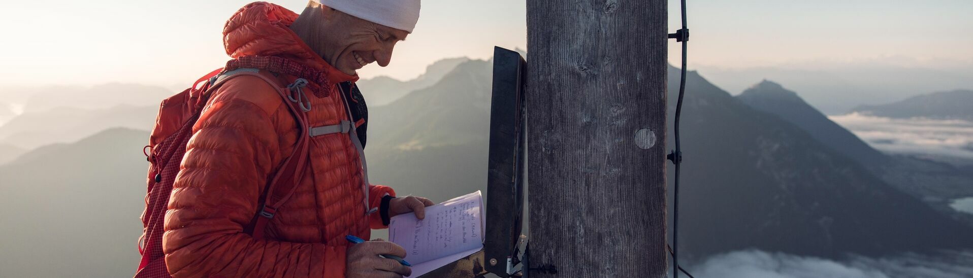 Ein Bergläufer der sich im Gipfelbuch der Seekarspitze im Karwendelgebirge einträgt bei einer schönen Aussicht auf die nebeligen Täler.