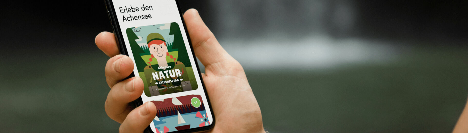 Ein Mann hält sein Handy in der Hand und hat die App der Wunderwege mit dem Achensee Naturerlebnispfad geöffnet.