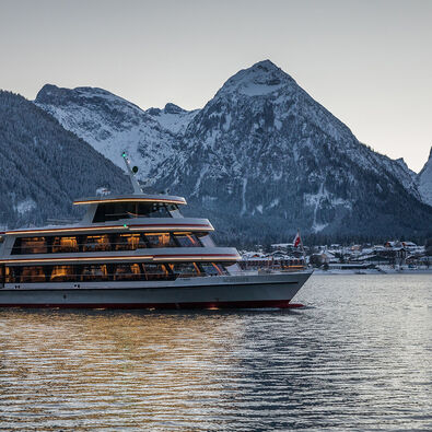 The MS Achensee cruising over Lake Achensee on a winter evening. In the background of this photo is the village of Pertisau and the Karwendel mountains.