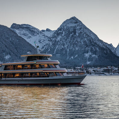 The MS Achensee cruising over Lake Achensee on a winter evening. In the background of this photo is the village of Pertisau and the Karwendel mountains.