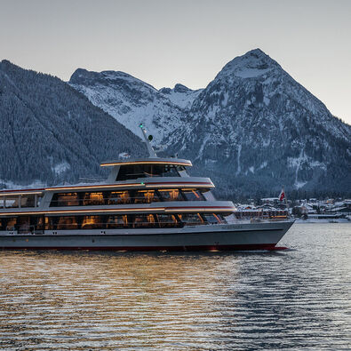 The MS Achensee cruising over Lake Achensee on a winter evening. In the background of this photo is the village of Pertisau and the Karwendel mountains.