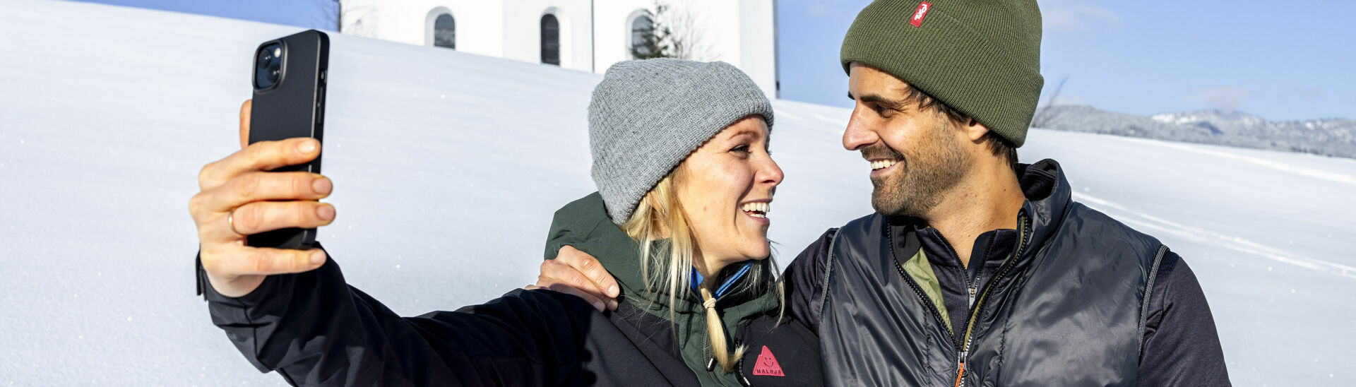 Winterzauber beim Annakircherl in Achenkirch am Achensee Ein Pärchen möchte den schönen Moment, umgeben von einer herrlichen Winterlandschaft und dem Annakircherl im Hintergrund, mit dem Handy festhalten.