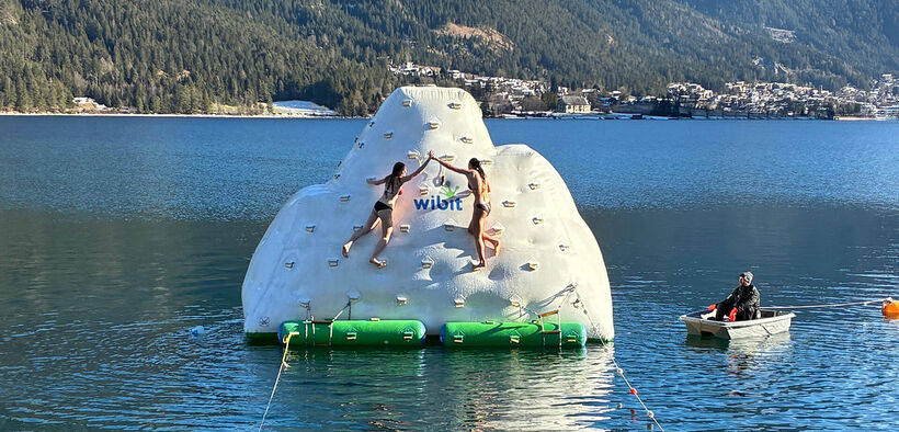 Beim Silvesterschwimmen am Achensee erklimmen zwei Teilnehmer bei herrlichem Wetter einen mit Luft gefüllten Eisberg und läuten die Glocke.