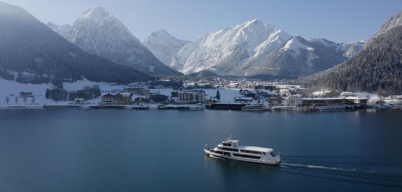 Die Achenseeschifffahrt gleitet über den See. Im Hintergrund das verschneite Pertisau am Achensee.