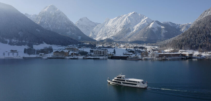 The Achensee boat glides across the lake. Snow-covered Pertisau am Achensee in the background.