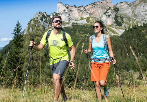 Ein Mann und eine Frau auf einer Wanderung im Rofangebirge durch schöne Wiesen und Felder.