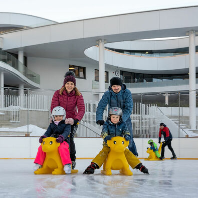 A family enjoys ice skating on the ice rink of the Atoll Achensee on a beautiful winter day.