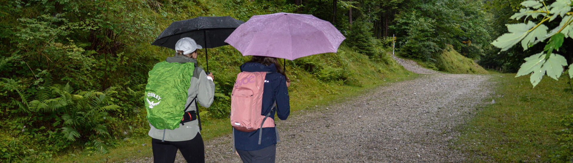 Zwei Frauen unternehmen eine kleine Wanderung am Besinnungsweg in Pertisau, mit Regenschirm, und genießen ihren Ausflug trotz des durchwachsenen Wetters.
