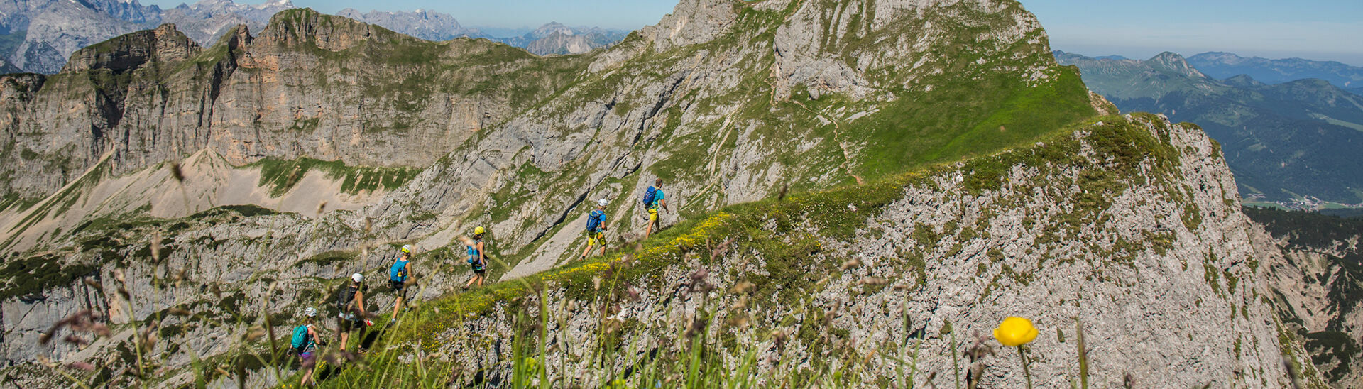 Eine Gruppe Klettersteigcampteilnehmer wandern in Richtung Hochiss bei strahlend blauem Himmel.