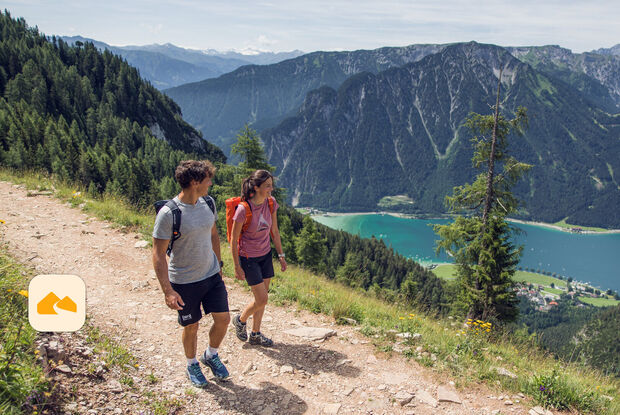 Wegepaten App Zwei Personen wandern auf einem schmalen Weg im Rofan. Im Hintergrund sind das Karwendelgebirge und der Achensee zu erkennen.