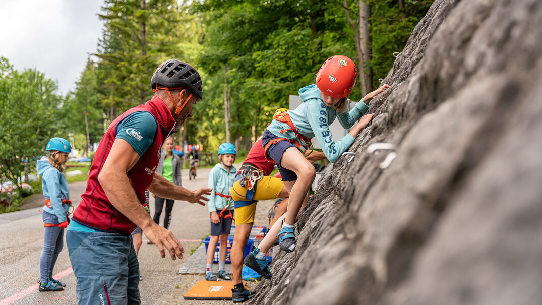 Eine Gruppe Jugendlicher die versuchen die 18 Meter hohe Kletterwand am Achenseehof mit Hilfe eines Guides zu erklimmen.