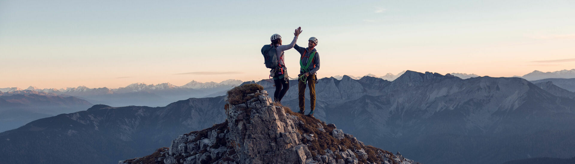 Zwei Kletterer klatschen miteinander am Gipfel des Gufferts bei leicht gerötetem Himmel ein.