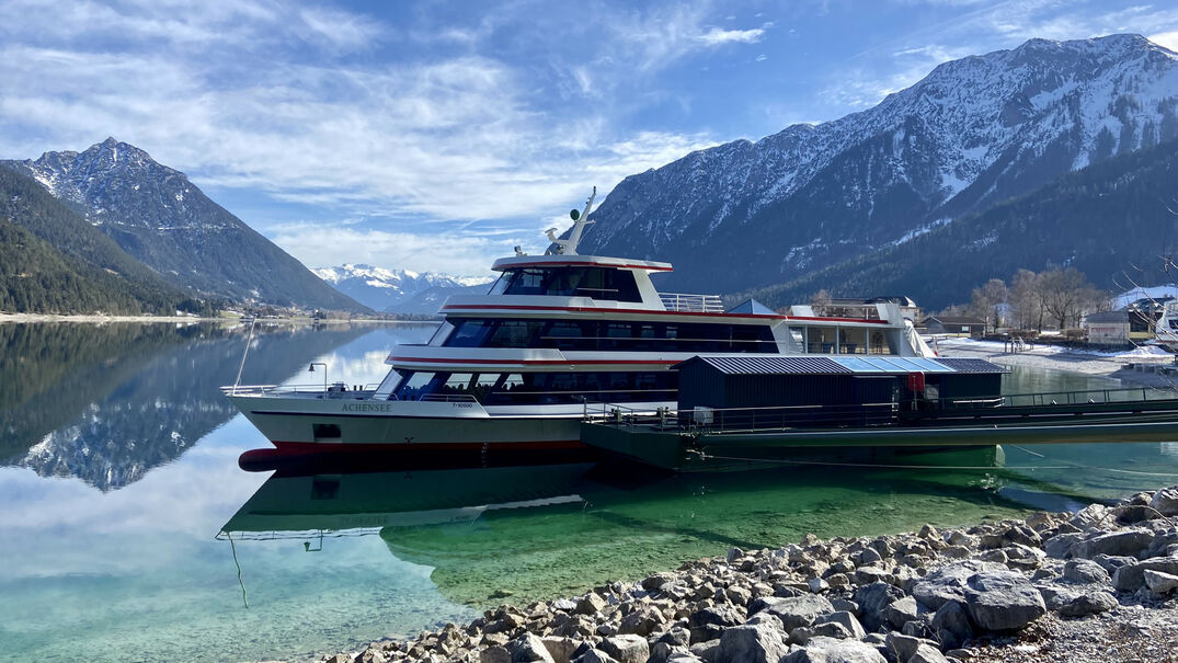 Die Achenseeschifffahrt legt hier in Pertisau am Achensee an. Im Hintergrund sind angezuckerte Berge wie das Ebner Joch zu sehen.