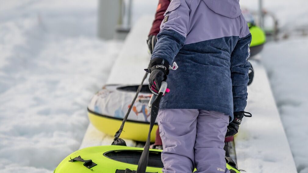 Zwei Kinder ziehen ihre Snowtubes durch den Schnee, bereit für die nächste Abfahrt.