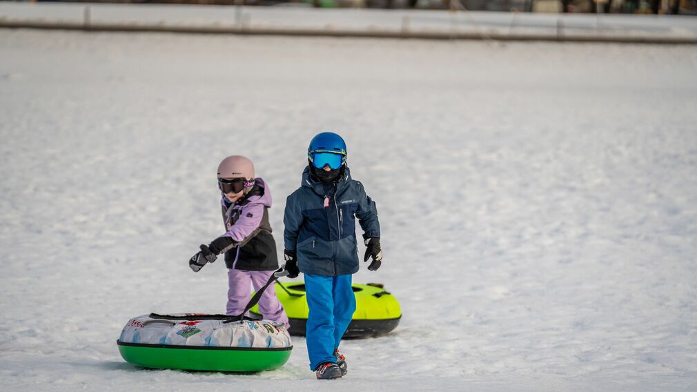 Zwei Kinder ziehen ihre Snowtubes durch den Schnee, bereit für die nächste Abfahrt.